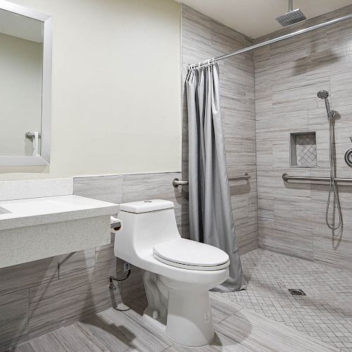 A modern bathroom with a walk-in shower, gray tiles, white toilet, sink with vanity, mirror, and towel racks on the walls ending the sentence.