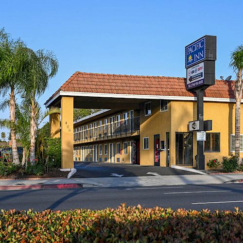This image shows a Motel Inn with a two-story building, palm trees, a sign, and a driveway entrance from the main road.