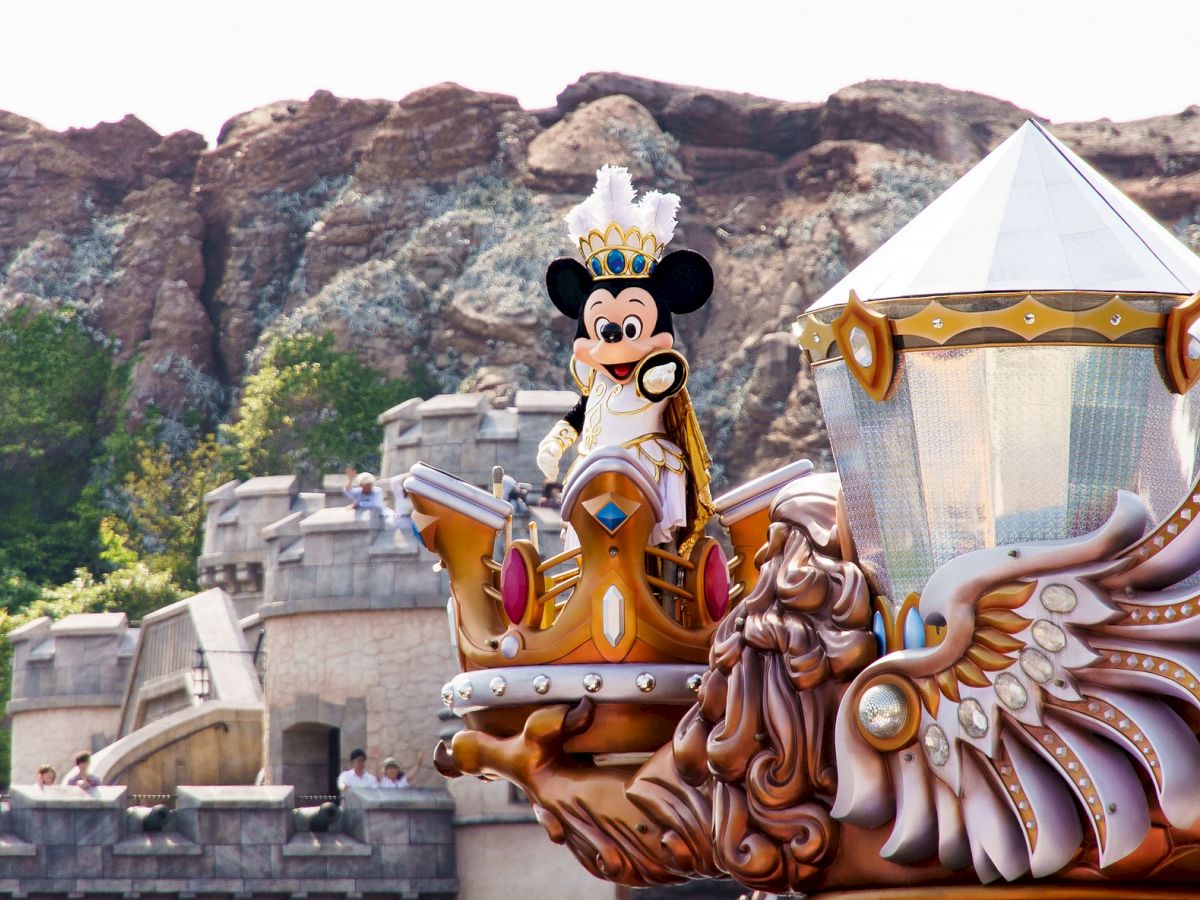 A large parade float features a costumed character wearing a crown, set against a rocky mountainous backdrop and castle-like structures.