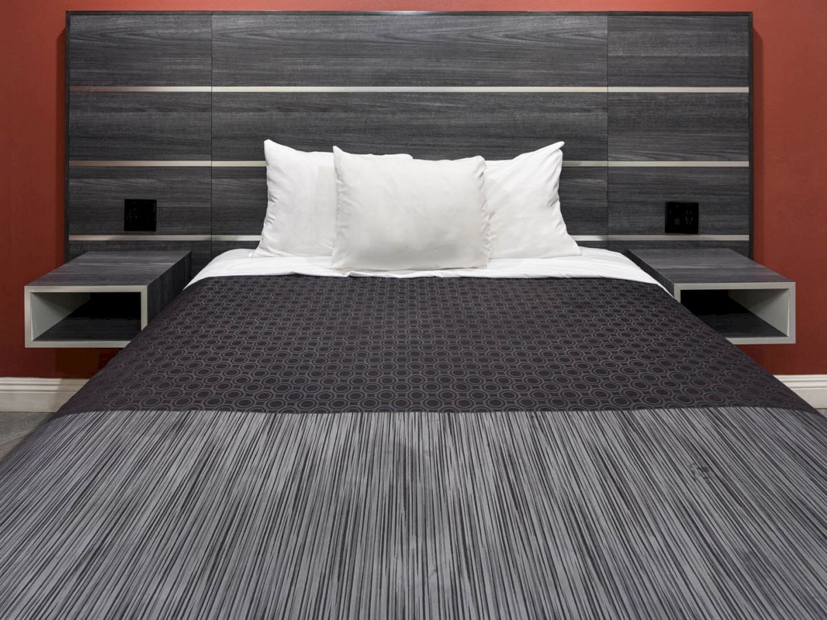 A modern bed with a black and grey headboard, white pillows, and a black bedspread in a room with red walls.